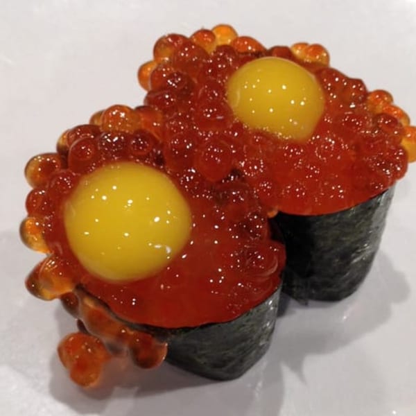 Two gunkan sushi pieces topped with bright orange salmon roe and a raw quail egg yolk.