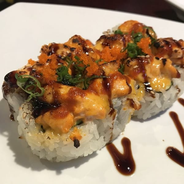 Sushi rolls topped with spicy sauce, orange tobiko, green onions, and a drizzle of dark sauce.
