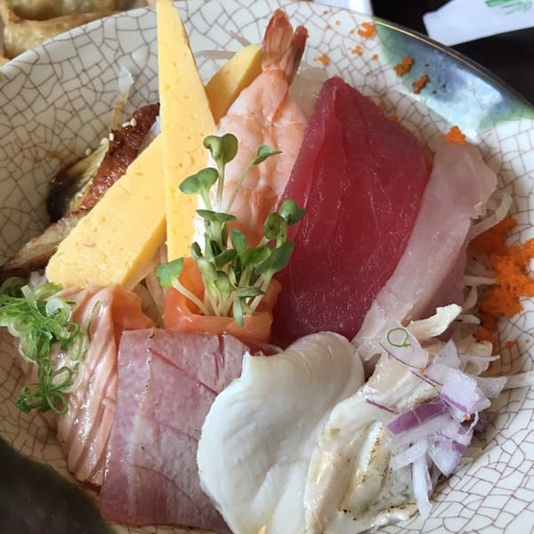 A colorful chirashi bowl from Sushi & Wok, featuring various sashimi, tamago, and shrimp over rice.