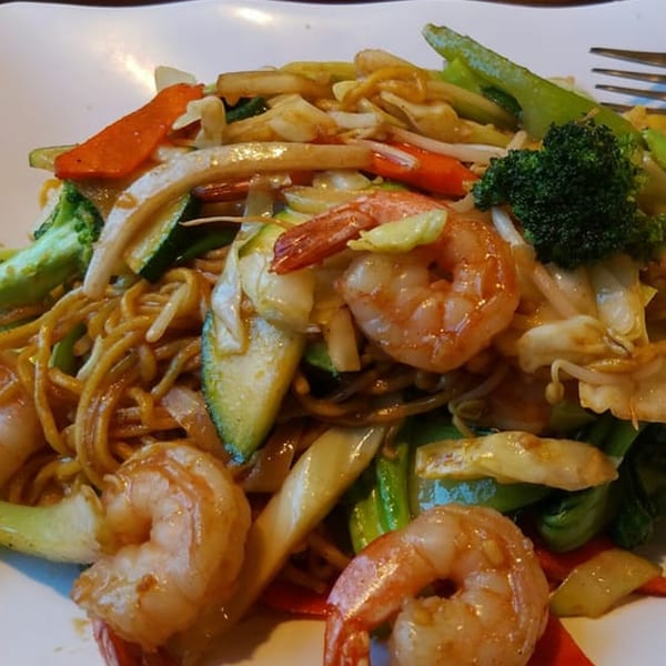 Shrimp lo mein with broccoli, zucchini, carrots, and other mixed vegetables on a white plate.